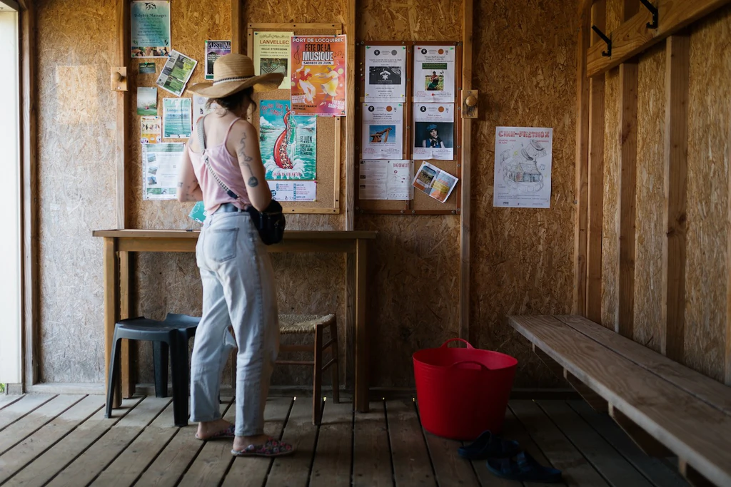 Femme de dos devant un panneau de prospectus dans un l'intérieur en bois d'un cabanon de plage